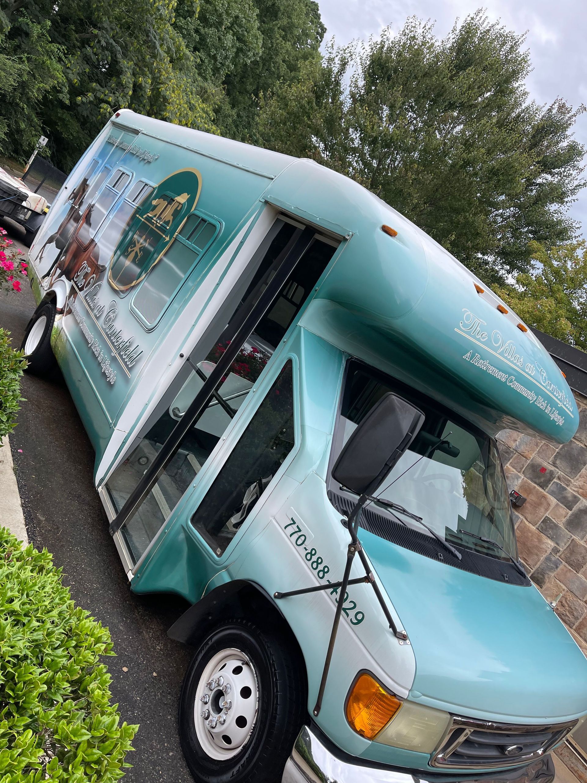 Blue and teal shuttle bus parked on a driveway with business logo.