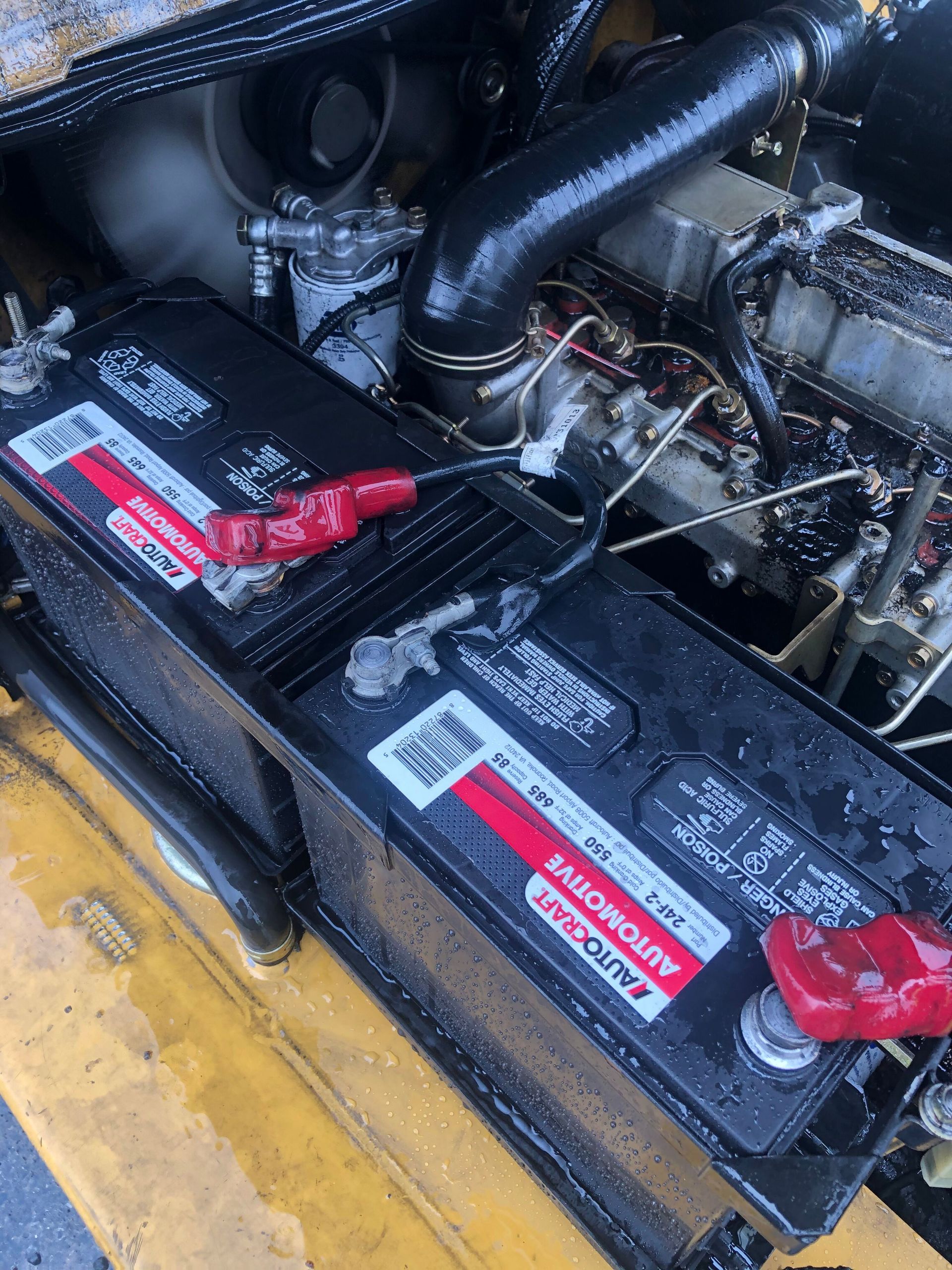 Two black car batteries in an engine compartment, red terminal protectors visible.