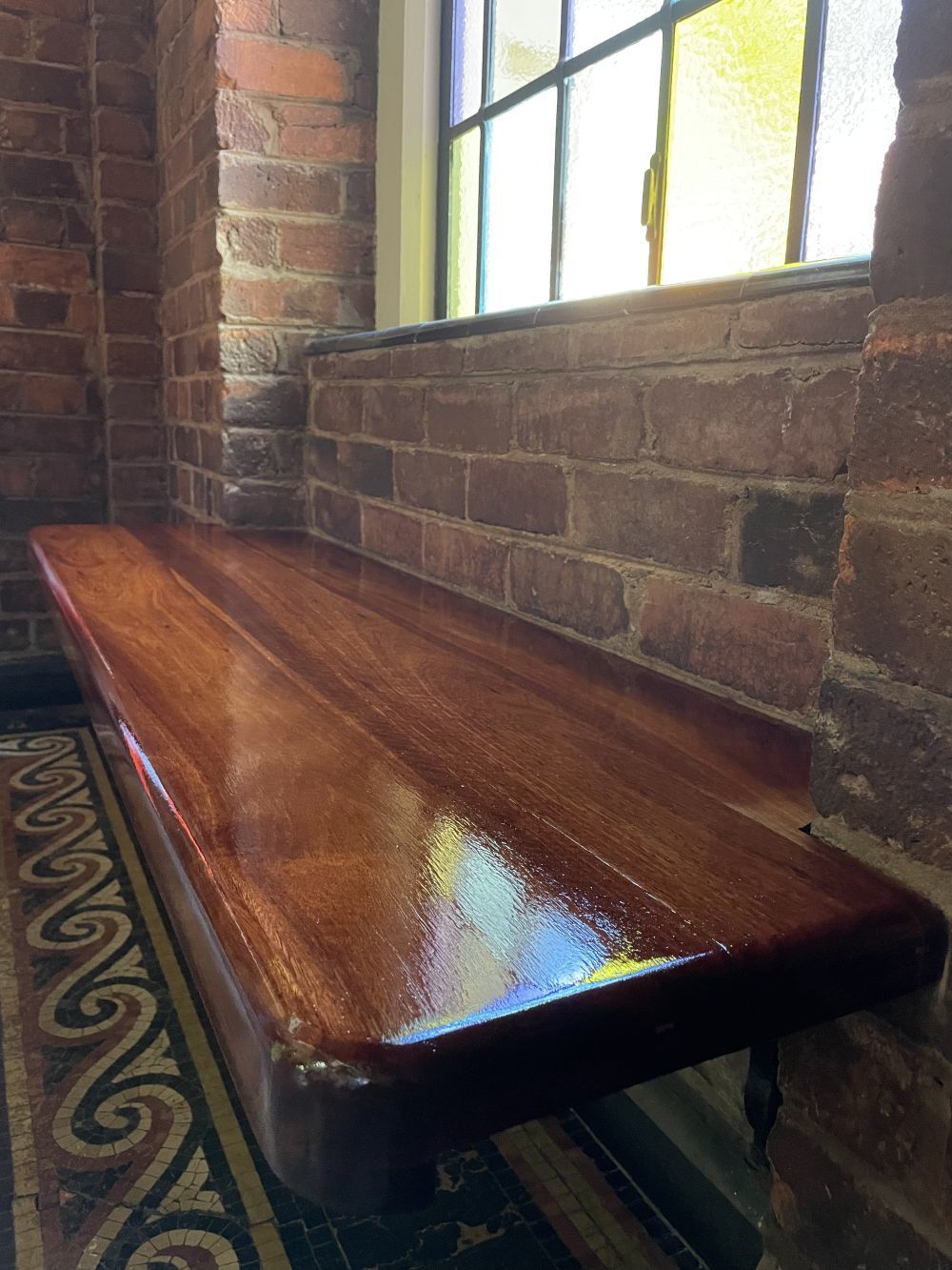 Wooden bench built into a brick wall beneath a window; interior, sunlight.