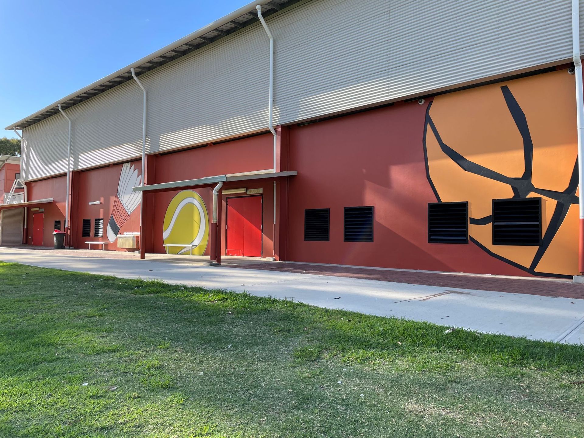 Fresh painted sports murals and a walkway, with grass in the foreground.