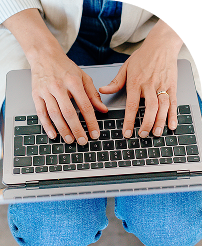 Hands typing on a laptop keyboard, wearing a white sweater and blue jeans.