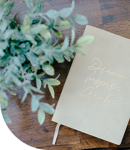 Gold notebook on wooden table beside eucalyptus sprig