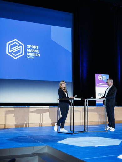 Two speakers on a blue-lit stage during the Sport Marke event