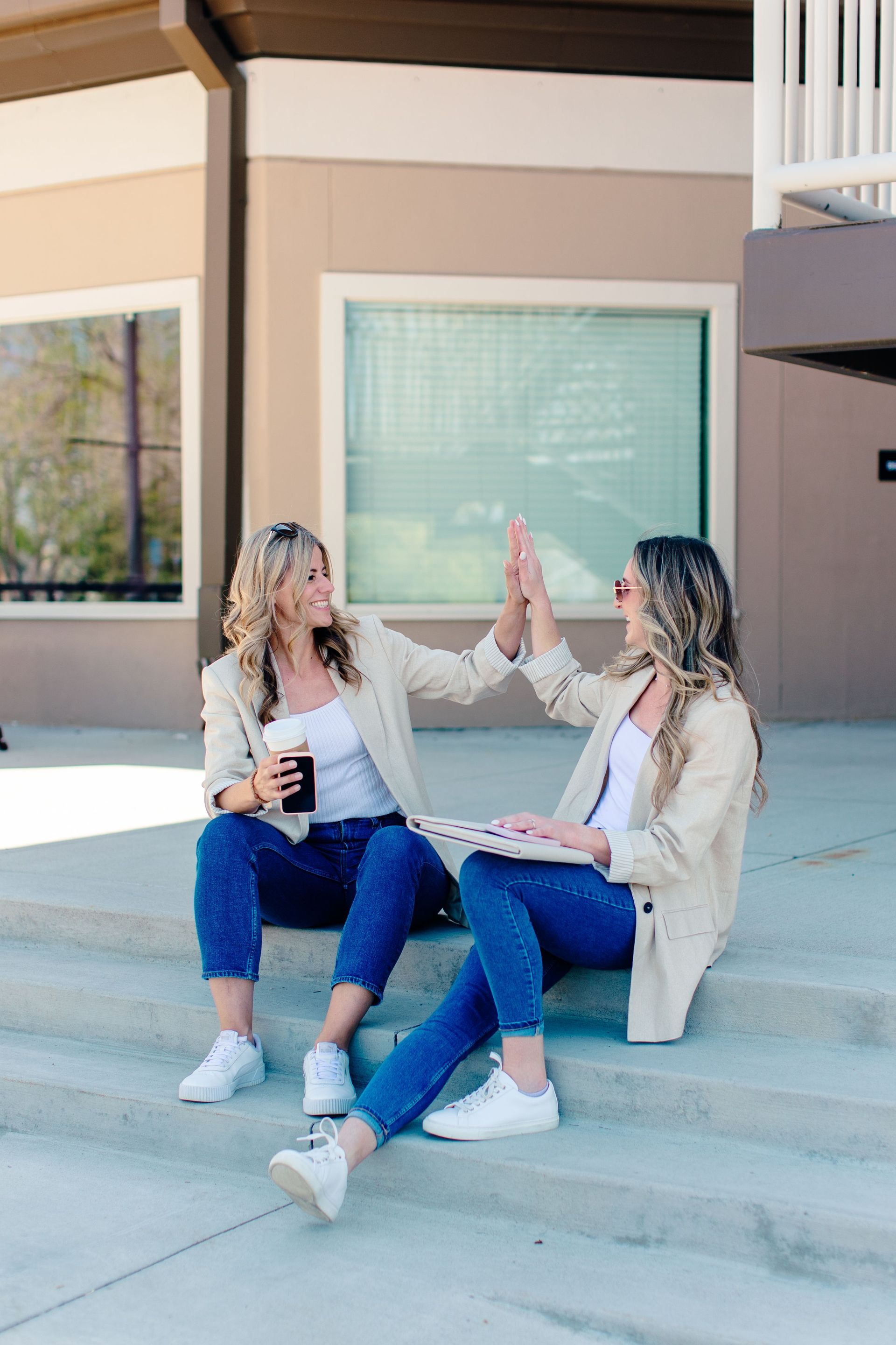 Two people sitting on steps, smiling and high-fiving outdoors with papers in hand