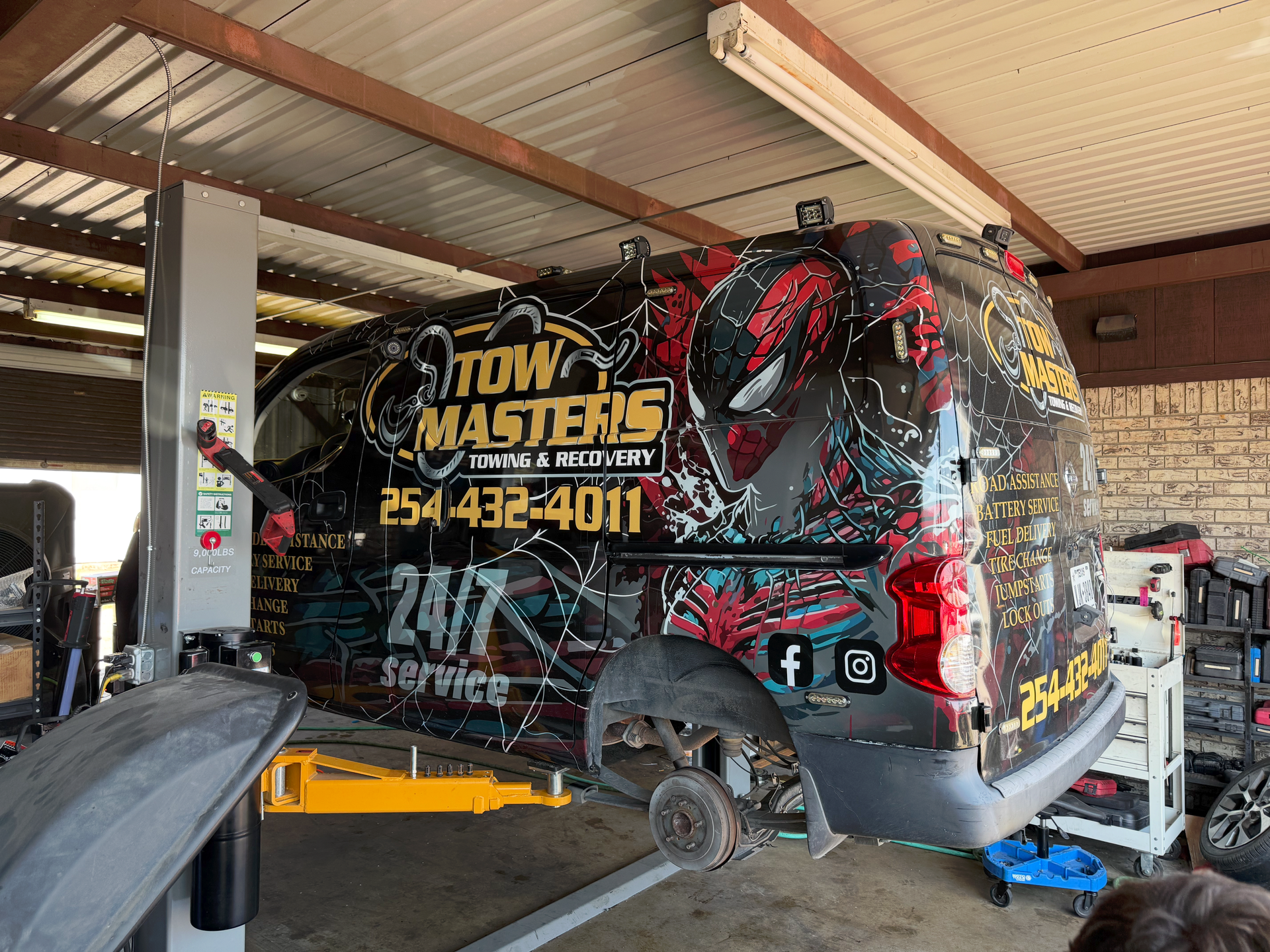 Tow Masters tow truck raised on a lift in a shop.  Black and red graphics, missing rear wheel. | Auto Masters Repair Shop