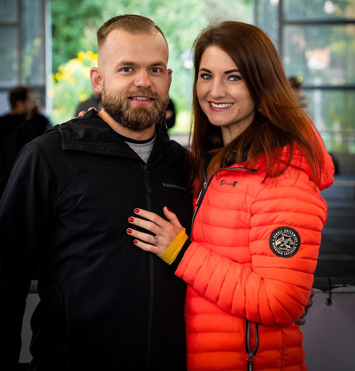 Ein Mann und eine Frau posieren für ein Foto. Die Frau trägt eine orangefarbene Jacke.