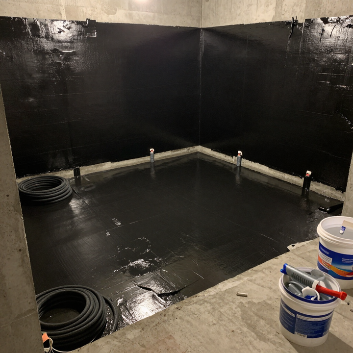 Freshly waterproofed basement in Renton, WA, showing dark protective wall coating and exposed plumbing.