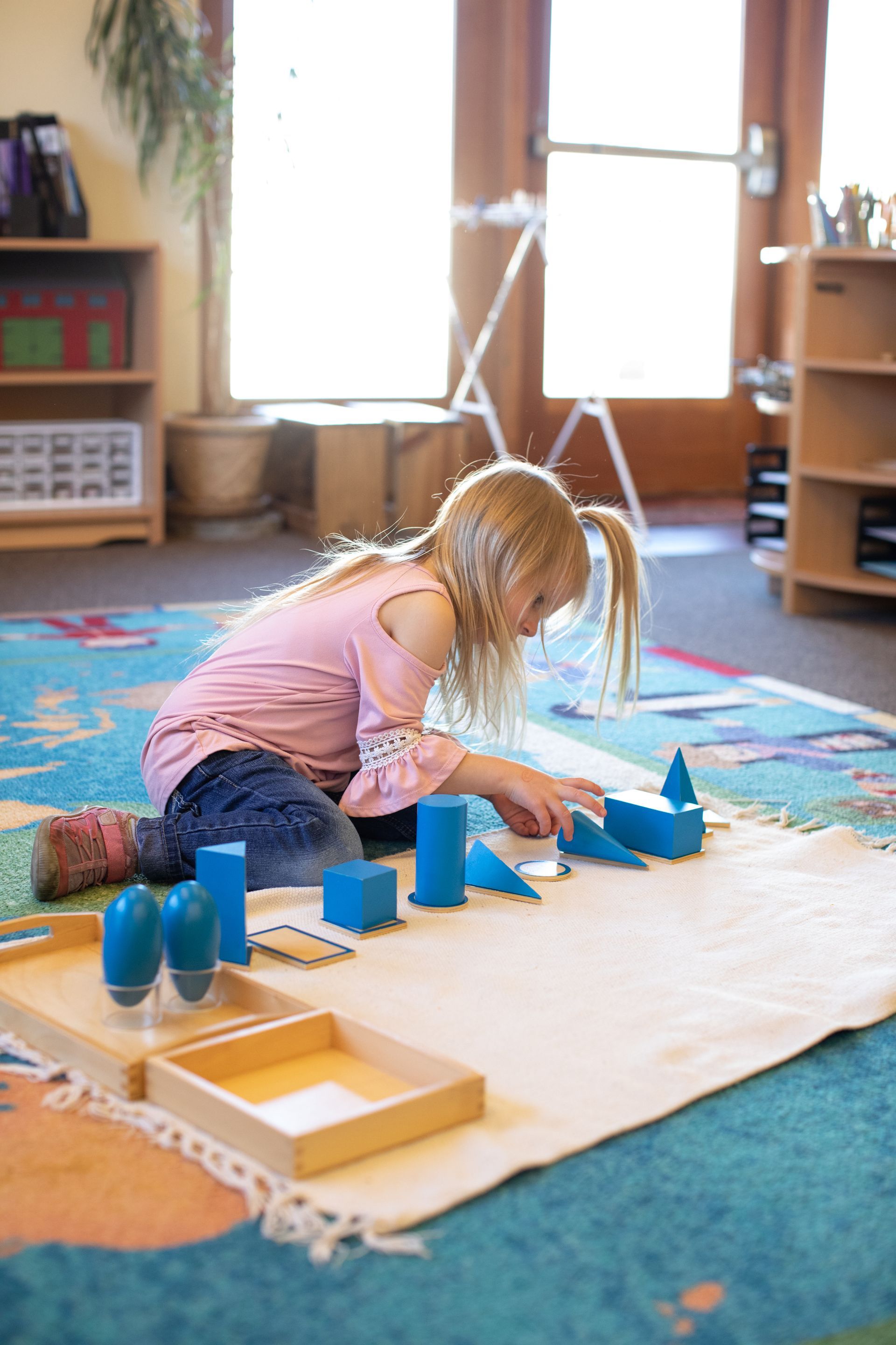 Child working with geometric solids on a rug near a sunlit window