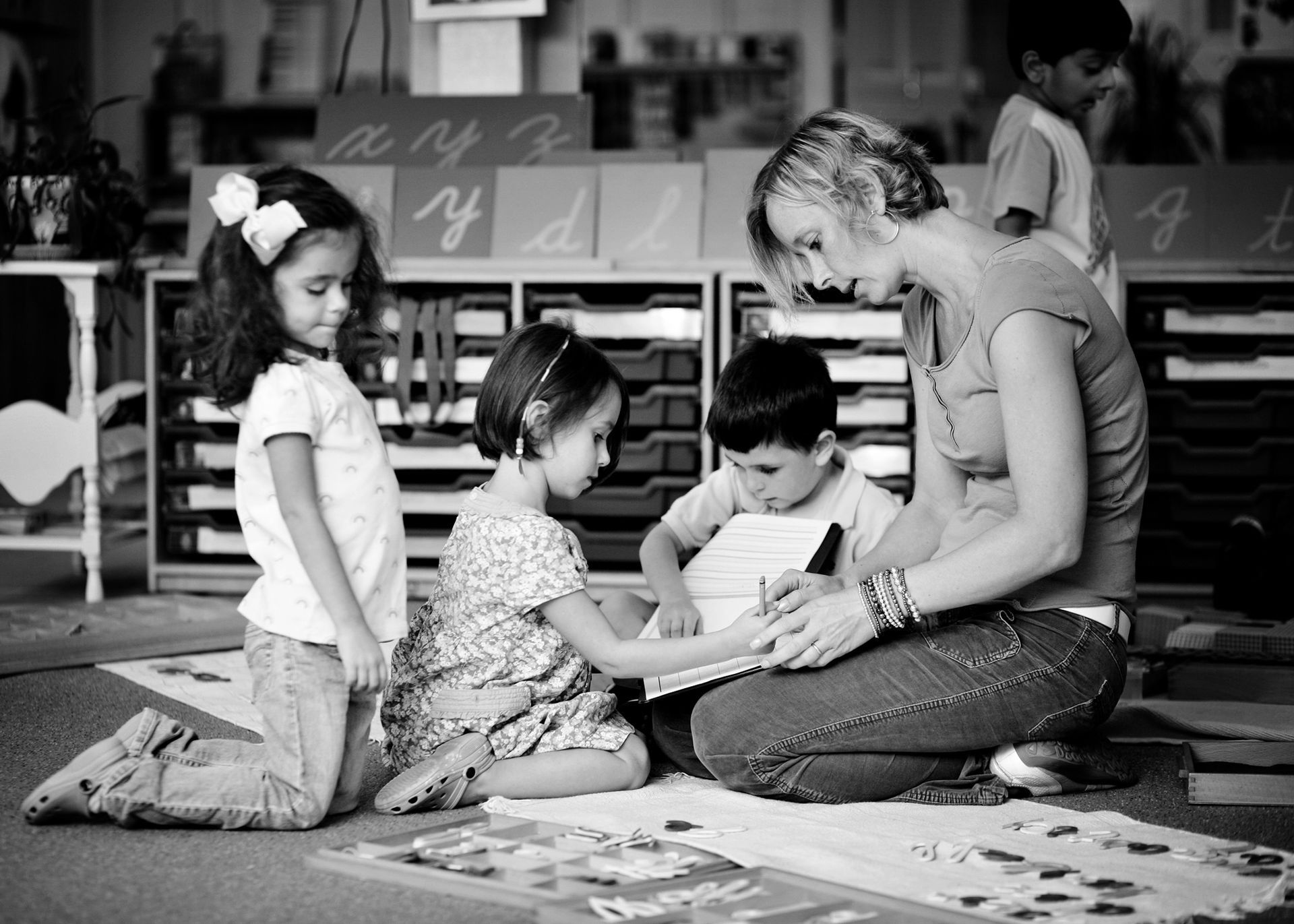 A Montessori teacher working with three young children in a classroom, focusing on a learning activity together.