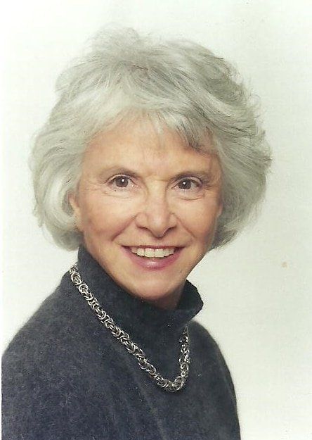 A woman wearing a turtleneck and a necklace smiles for the camera