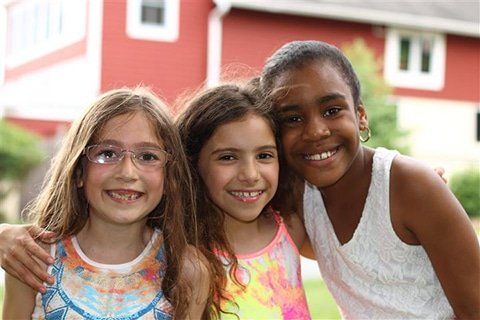 Three young girls are posing for a picture in front of a red barn.