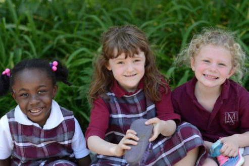 Three young girls in school uniforms are sitting next to each other.