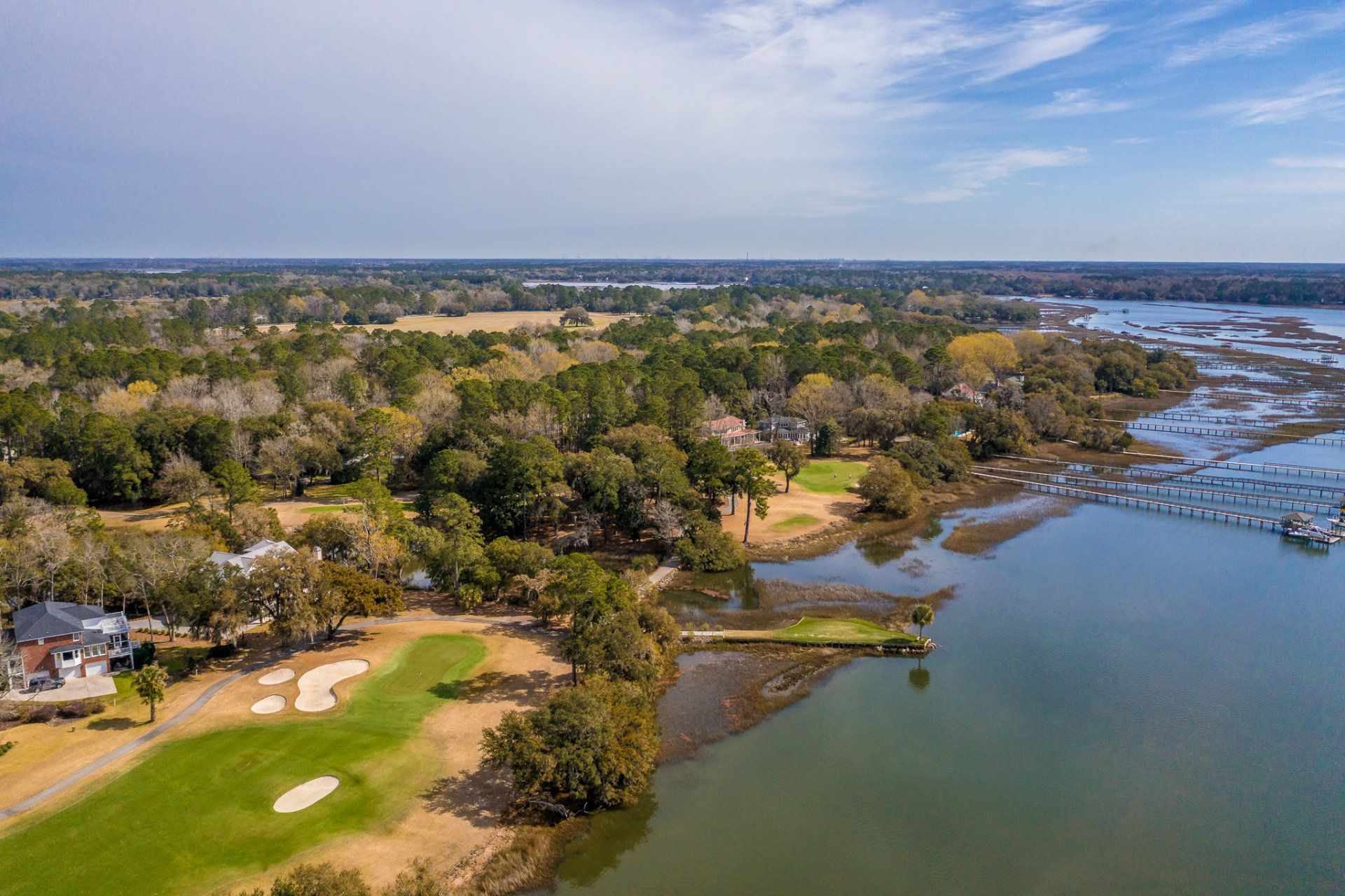 Aerial view of a riverside golf course beside a marina and scattered houses under clear skies