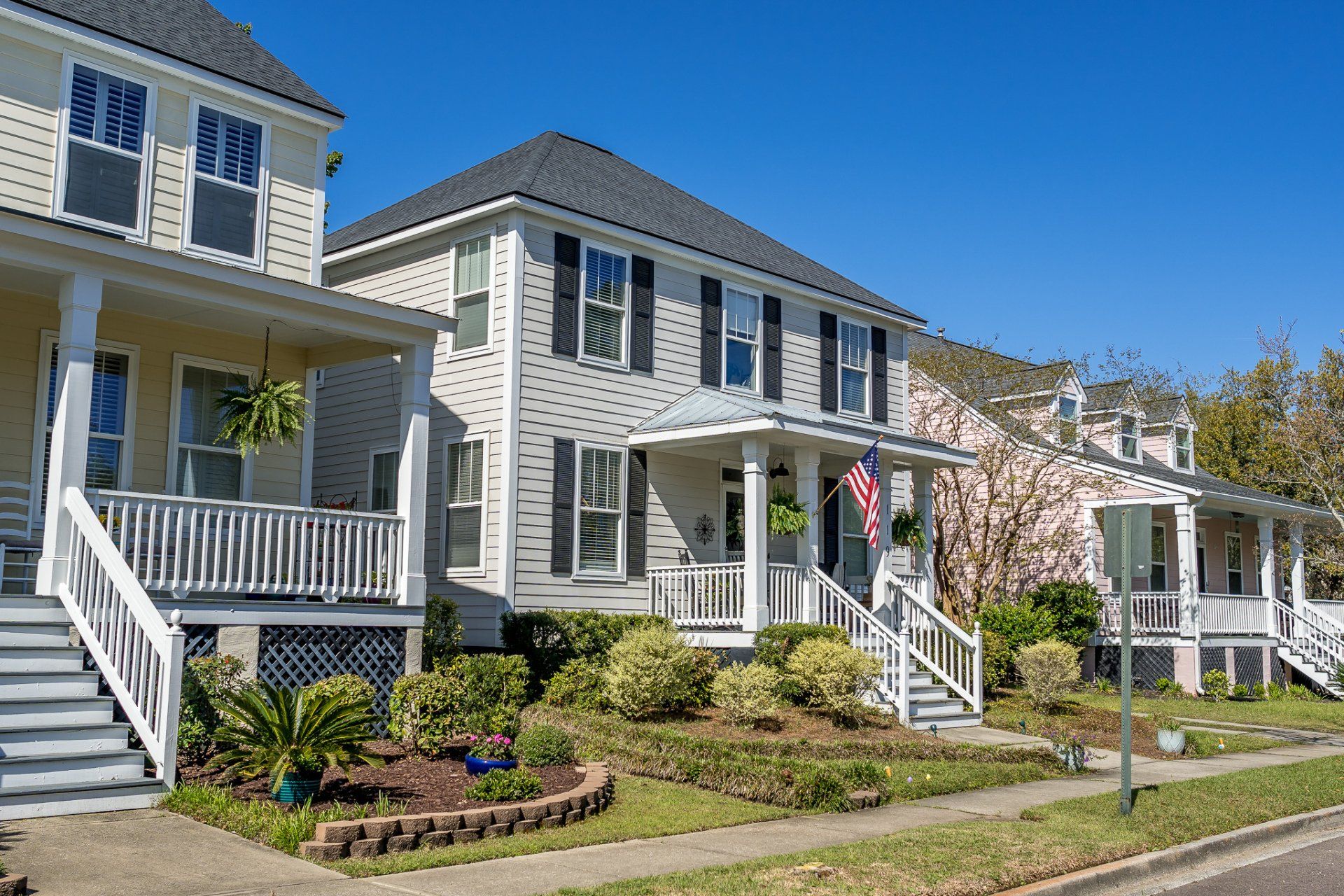 Row of gray-and-white townhouses with porches along a sunny street