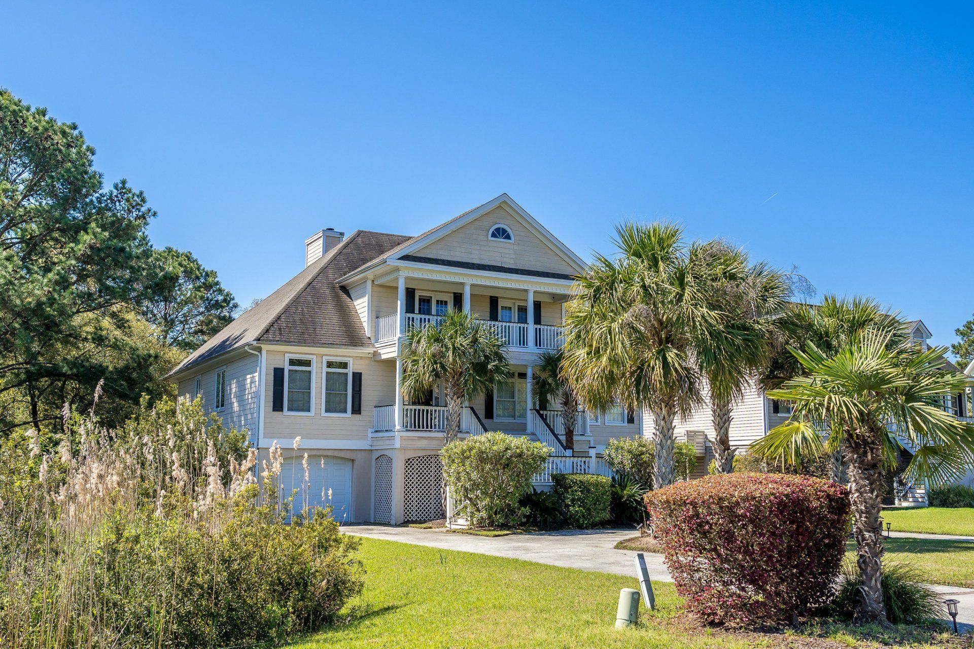 White house with a wraparound porch, palm trees, and landscaped yard under a clear blue sky
