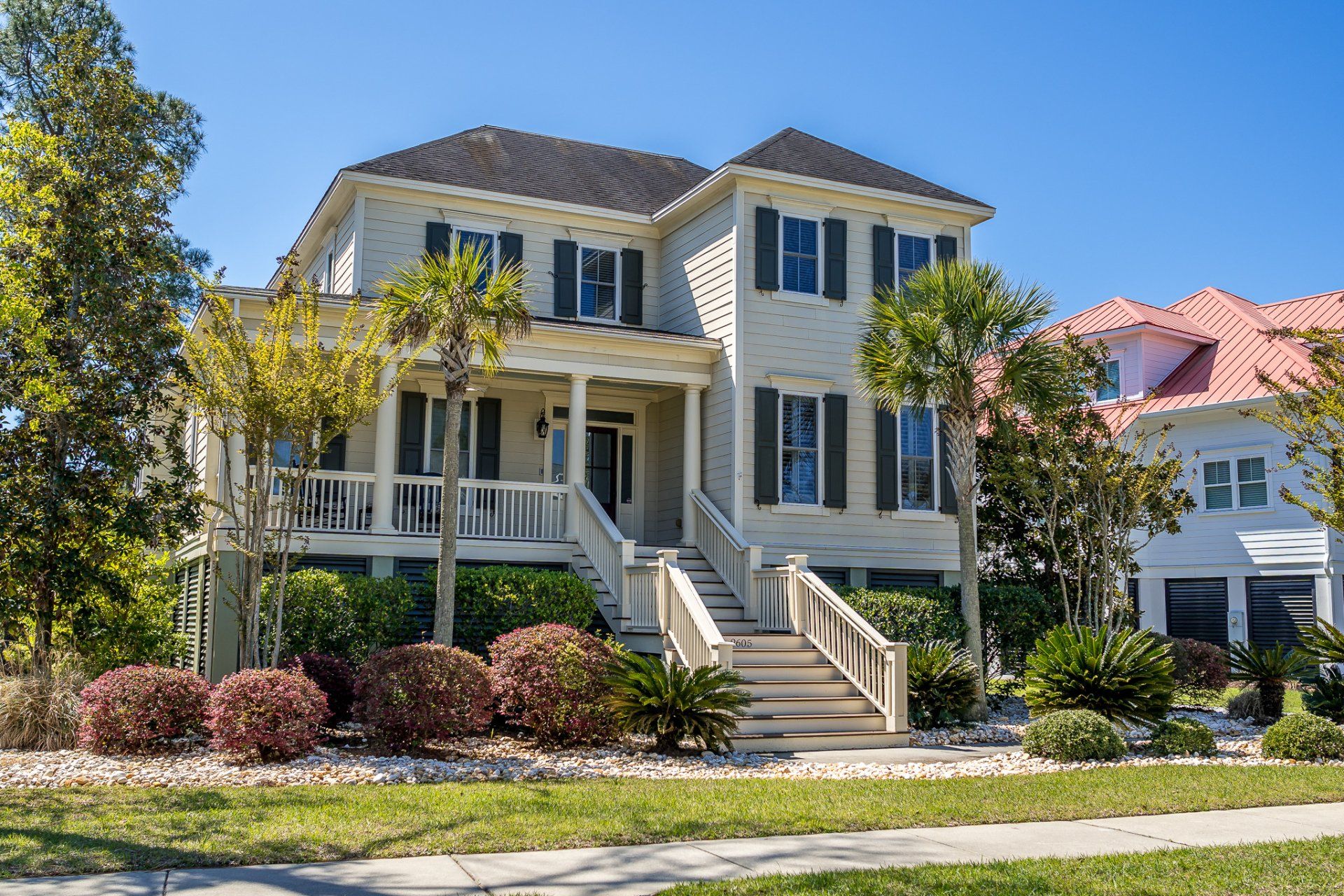 Victorian-style two-story house with beige siding, white trim, front porch, and landscaped yard under a clear blue sky