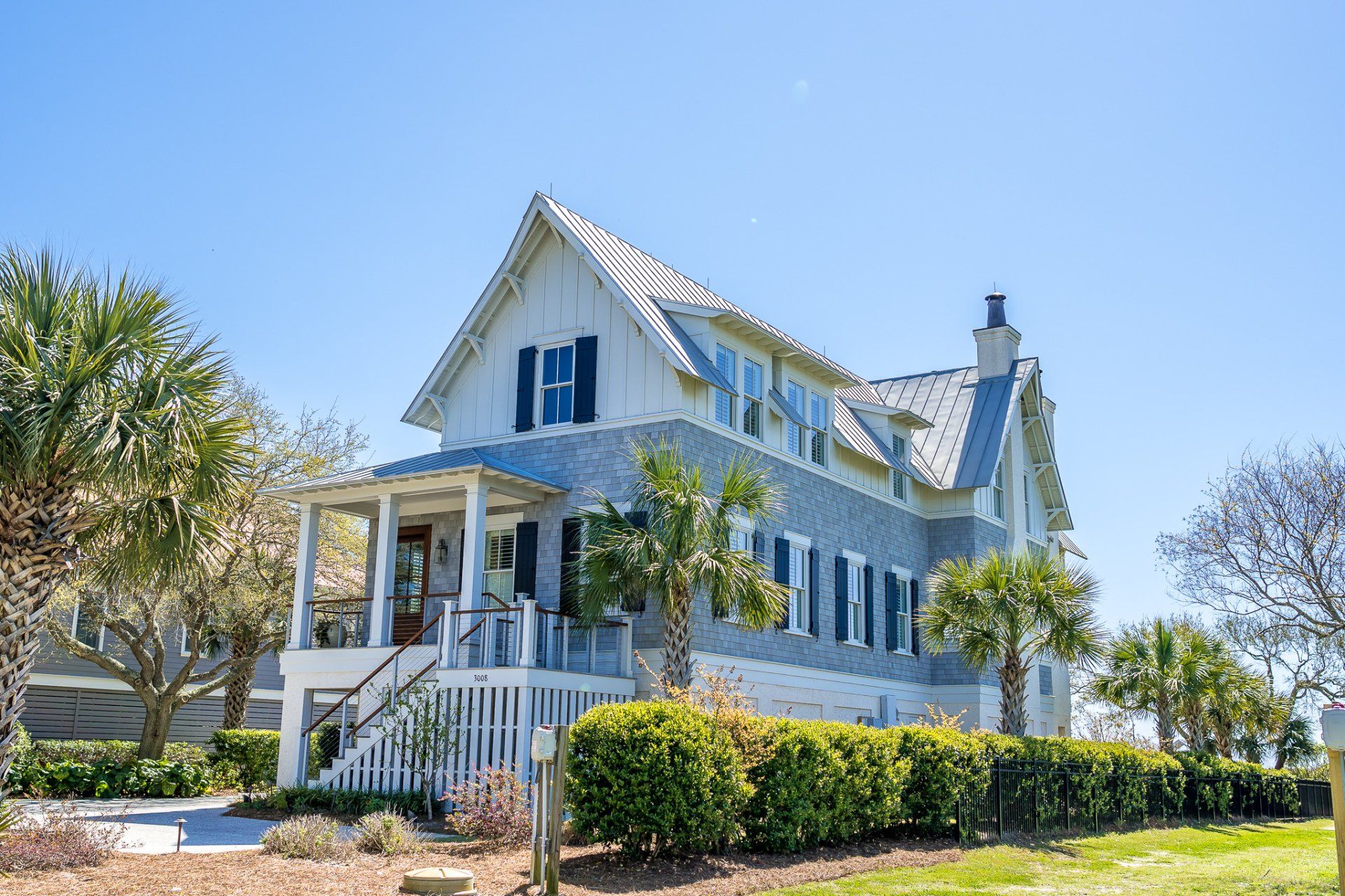 White Victorian house with blue shutters, porch, and palm trees on a sunny day
