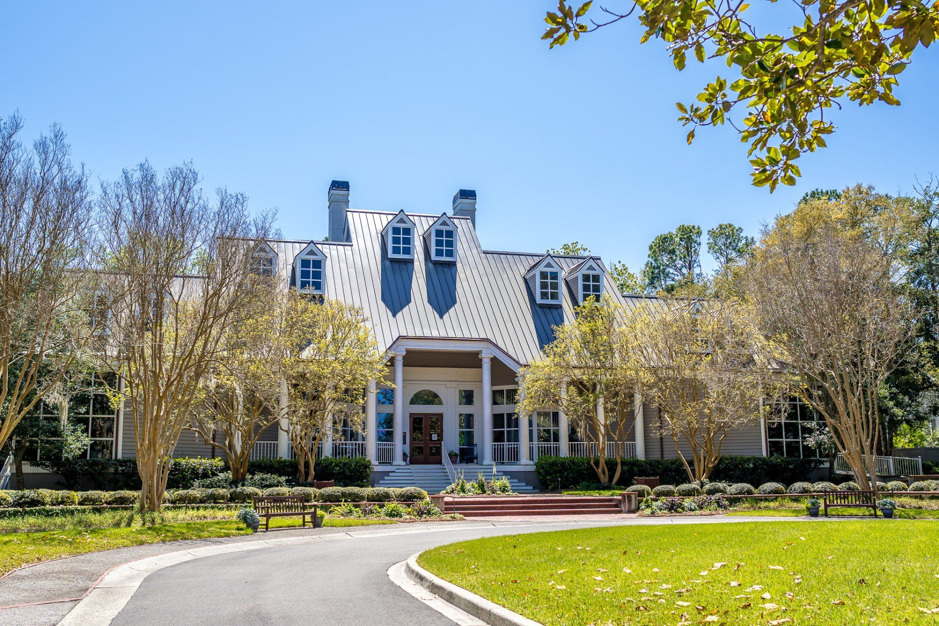 Large white house with blue dormers, arched entry, and a curved driveway surrounded by trees and lawn