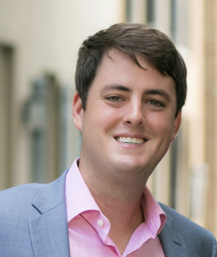 Smiling man in a light blue blazer and pink shirt outdoors