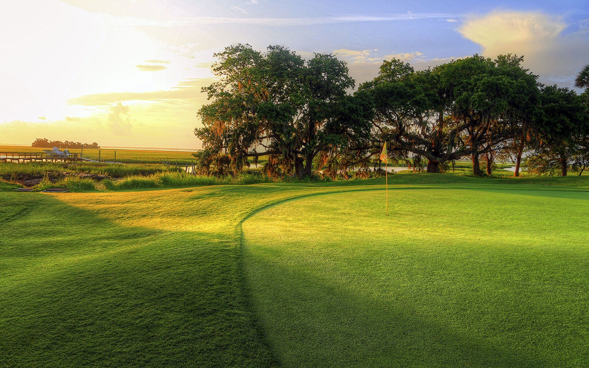 Sunlit green field with a curved path, trees in the distance, and a warm sky at sunset