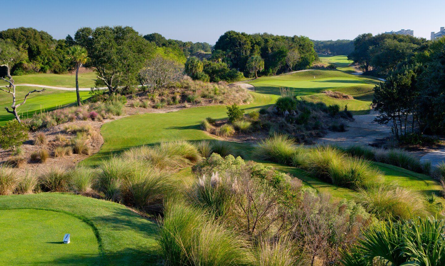 Lush green golf course with fairways, sand traps, and trees under a clear blue sky