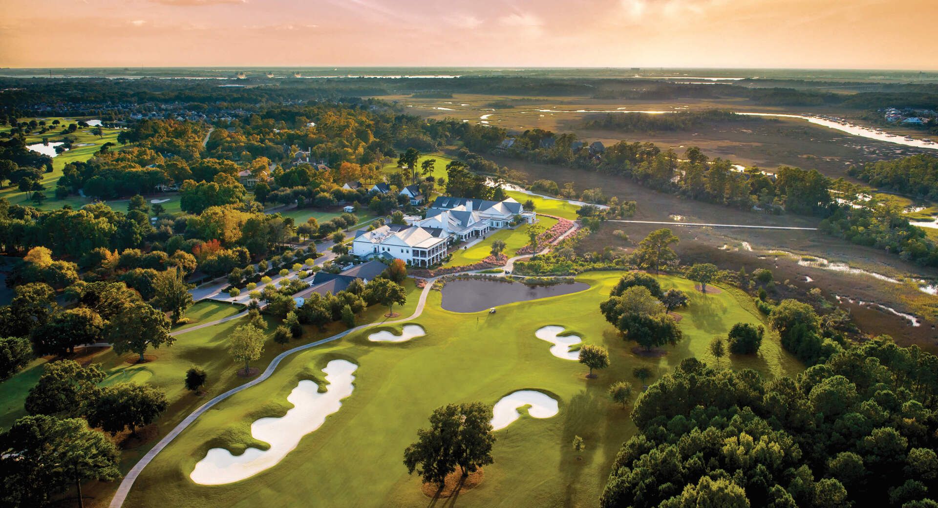 Aerial view of a golf course with sand bunkers, lush green fairways, and a clubhouse at sunset