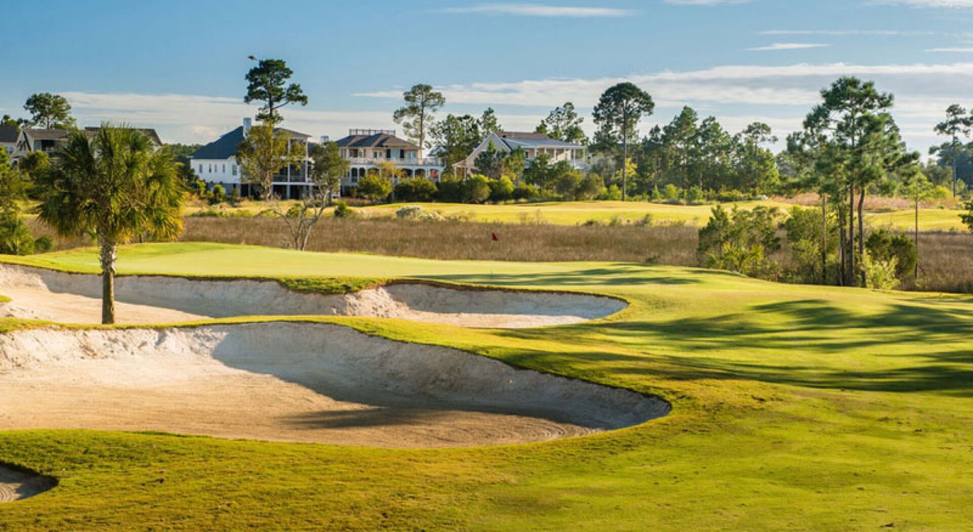 Golf course green with sand bunkers, trees, and a pond under a bright sky