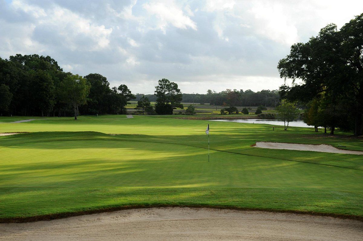 Golf course with green fairway, sand bunker, and trees under a cloudy sky