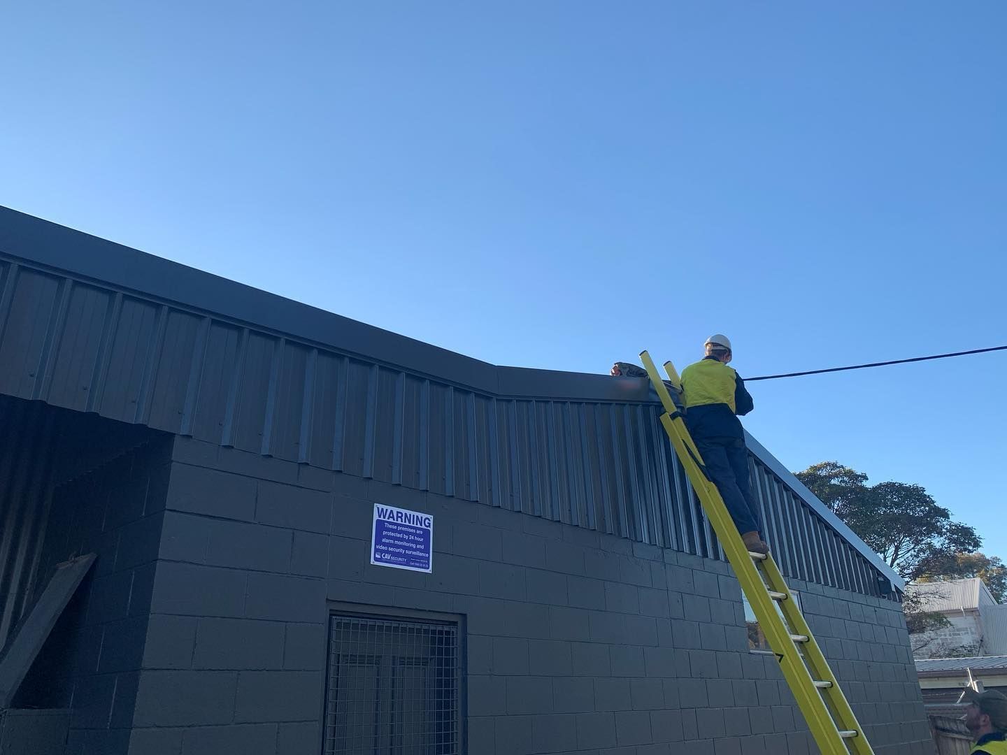 A Man is Standing on a Ladder on the Side of a Building — Northern Rivers Metal Roofing PTY LTD In Mullumbimby, NSW