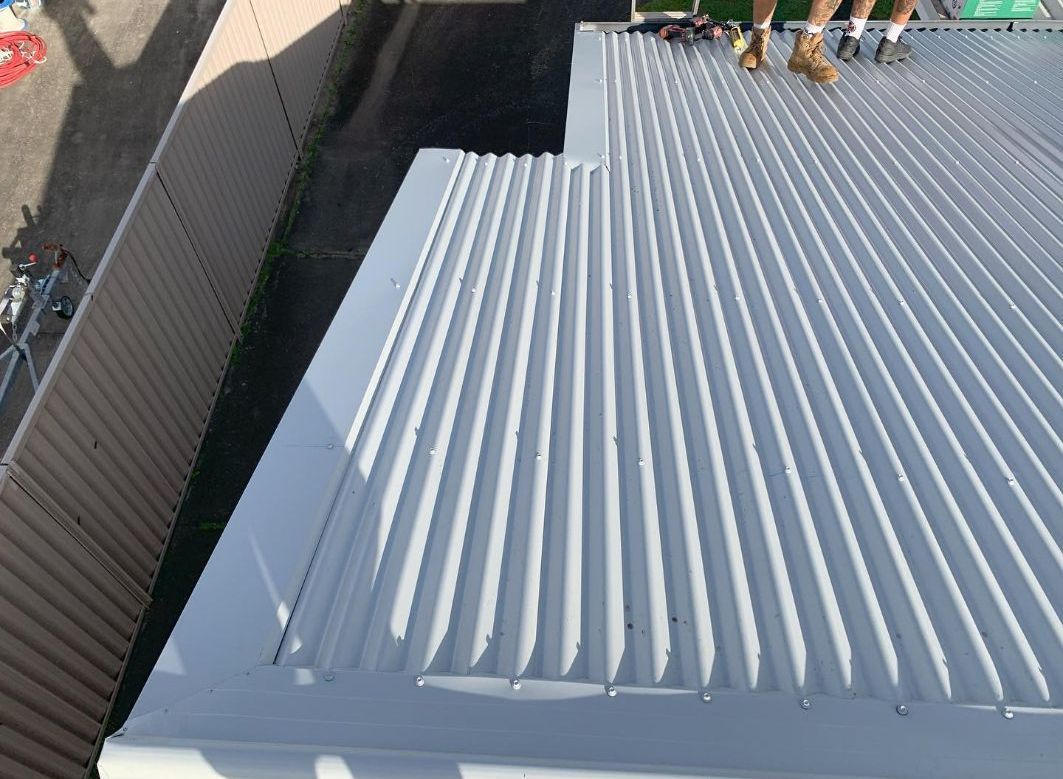 A Person is Standing on the Roof of a Building — Northern Rivers Metal Roofing PTY LTD In Byron Bay, NSW