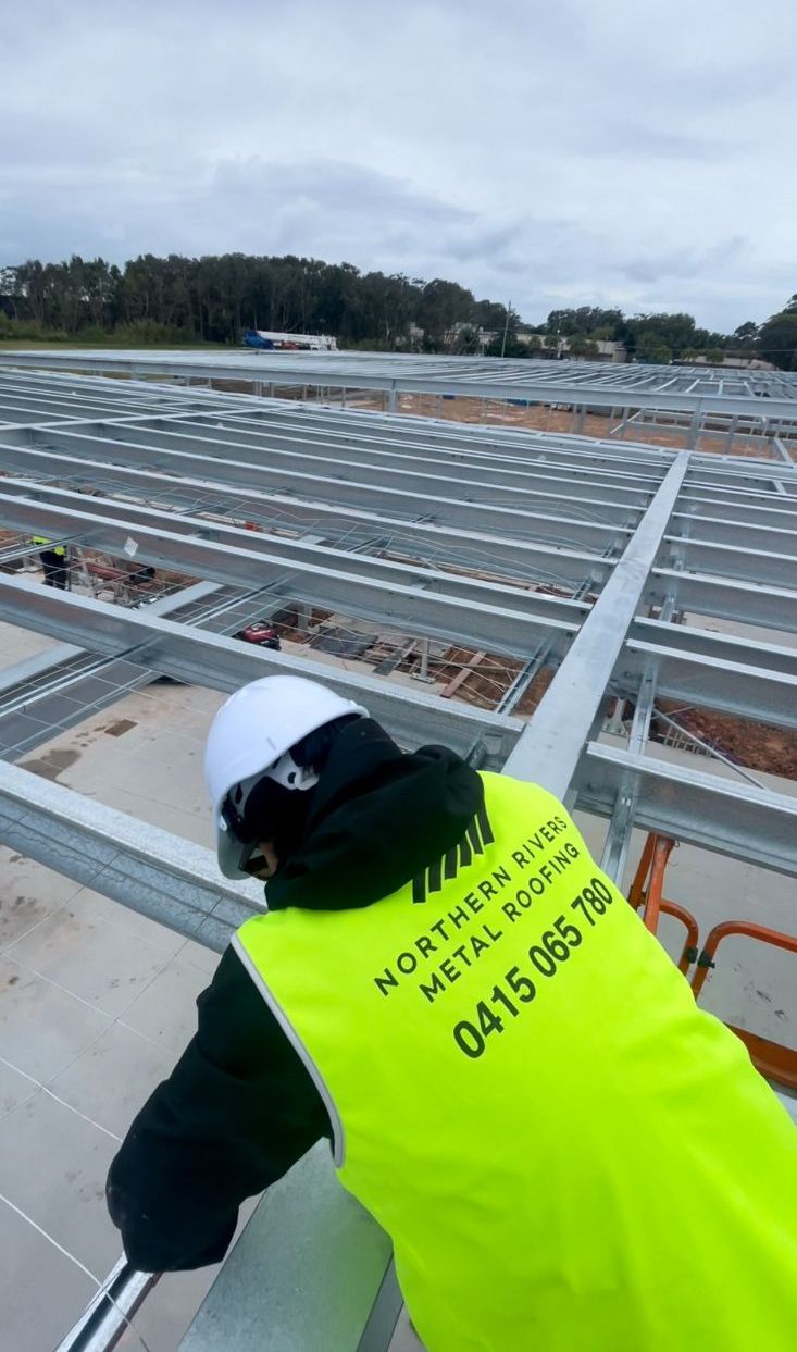 A Man in a Yellow Vest is Working on a Metal Structure — Northern Rivers Metal Roofing PTY LTD In Ewingsdale, NSW