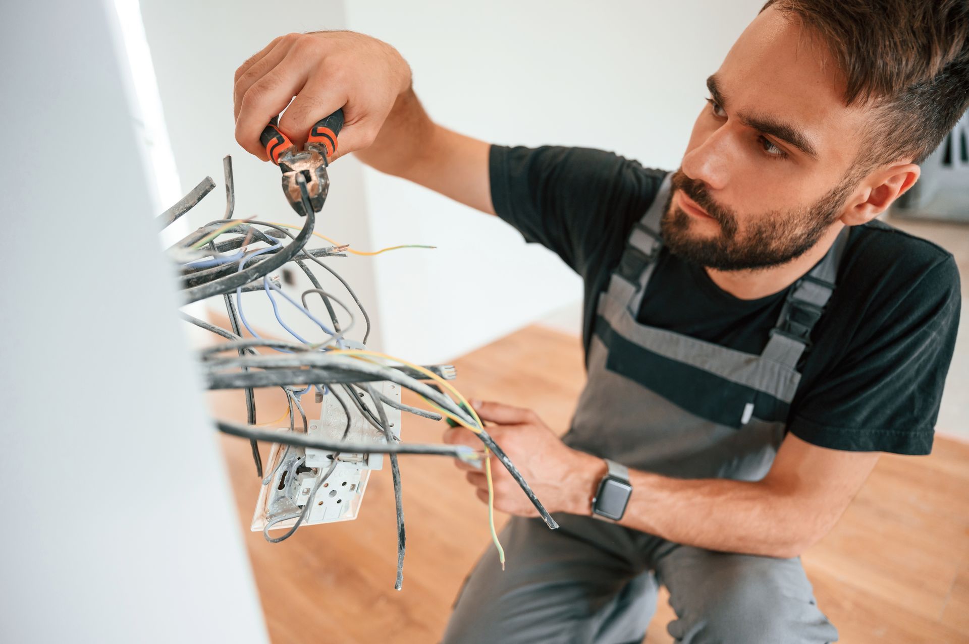 Technician wiring an electrical panel with exposed cables in a bright room