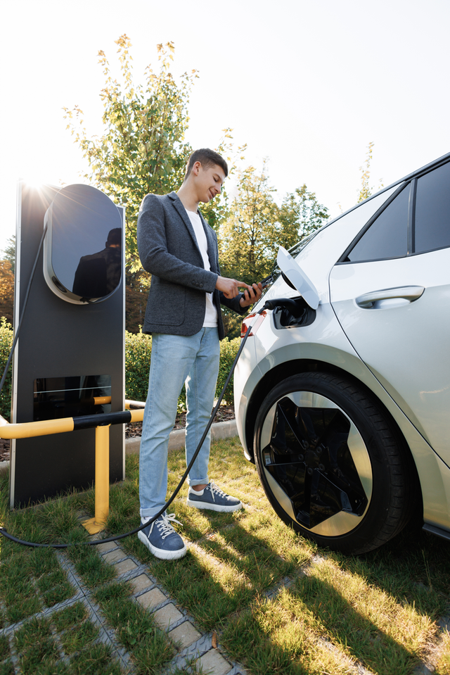 a man is charging his electric car at a charging station .