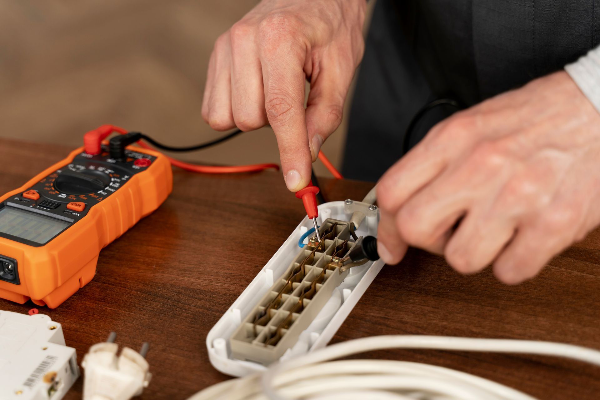 Hands testing a power strip with a multimeter on a wooden table