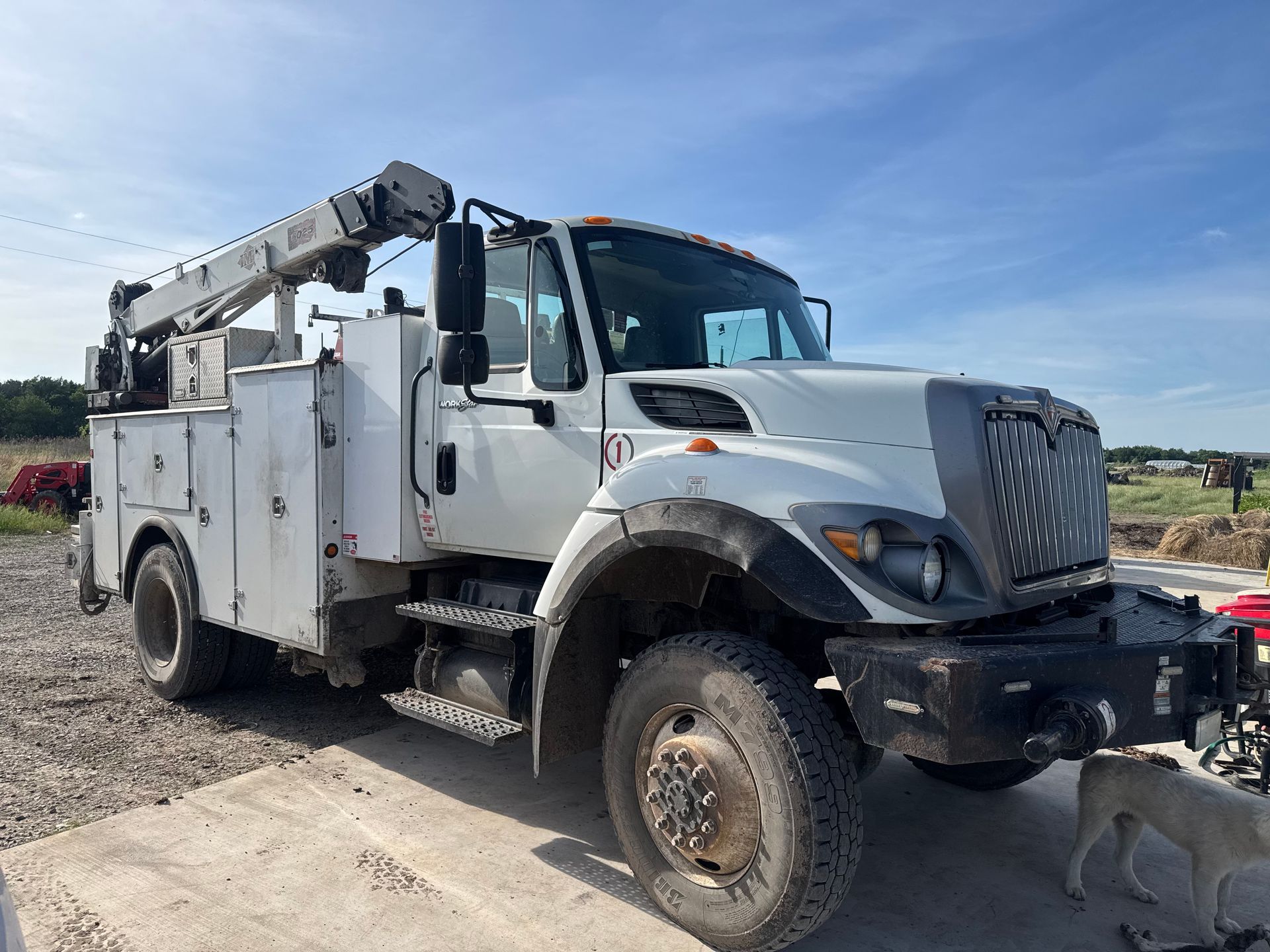 White utility truck with mounted boom parked on a dirt lot under a blue sky