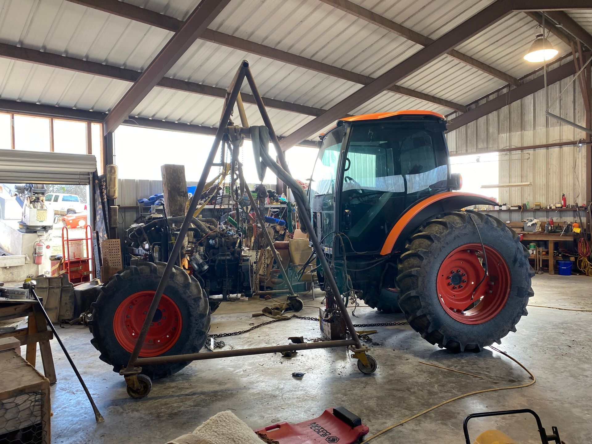 Tractor inside a farm workshop, partially disassembled with a front loader frame and red wheels.