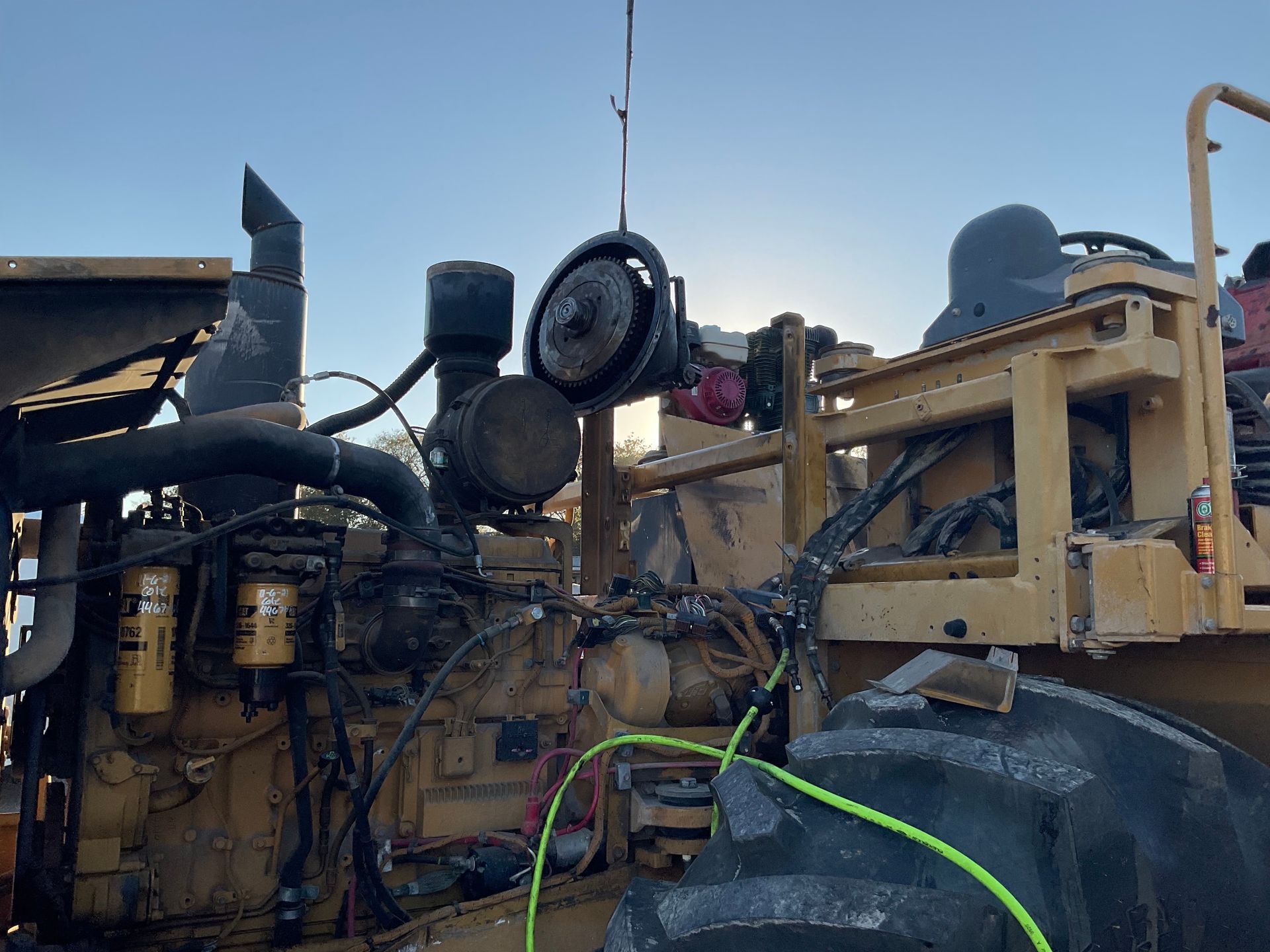 Yellow construction vehicle with a large tire and exposed engine parts against a blue sky