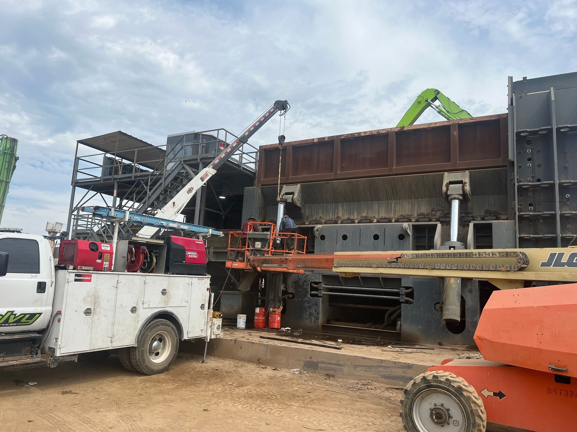 Construction site with a truck-mounted crane lifting steel beams beside a large industrial structure
