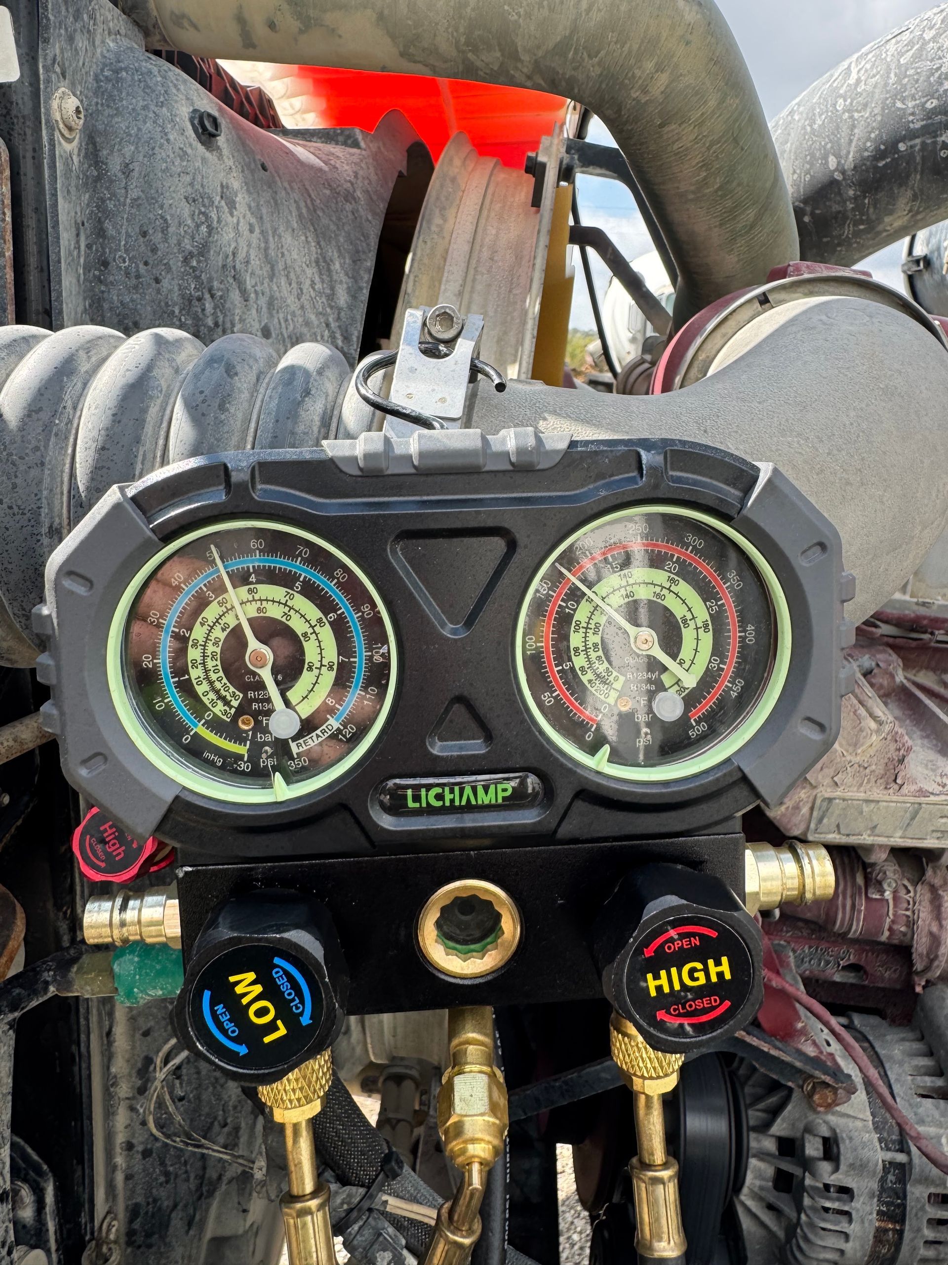 Close-up of a dual gauge A/C manifold set with blue and red hoses on an engine bay.