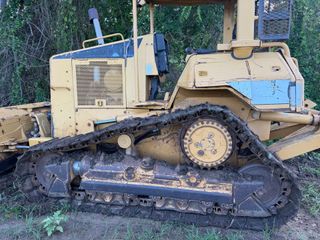 Yellow tracked bulldozer parked outdoors on dirt and grass, with a raised blade and weathered body.