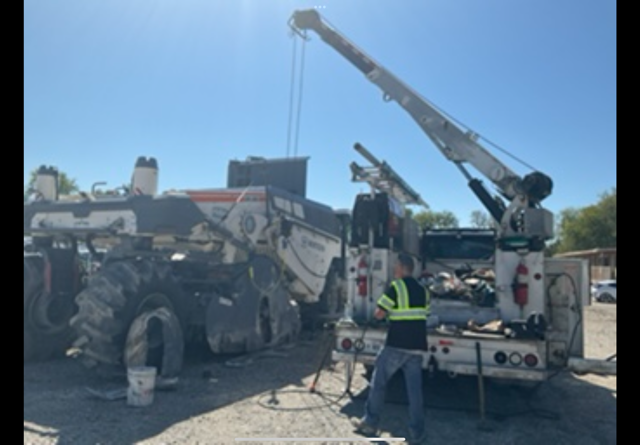 Construction site with a crane lifting equipment beside a large loader and a worker in a safety vest.