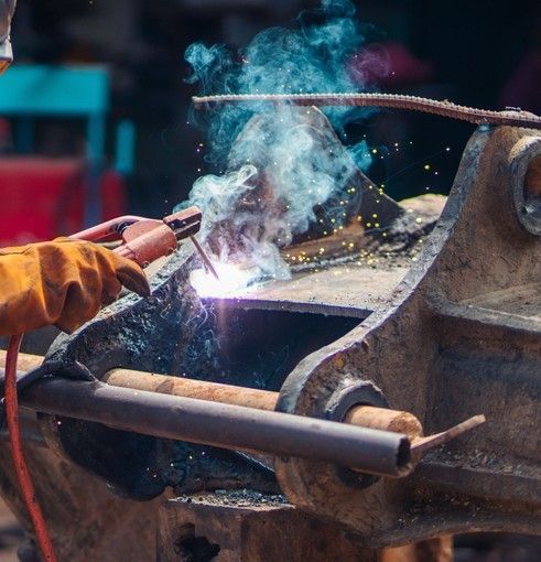 Welder using a torch on a metal pipe, with bright sparks and smoke at a workshop