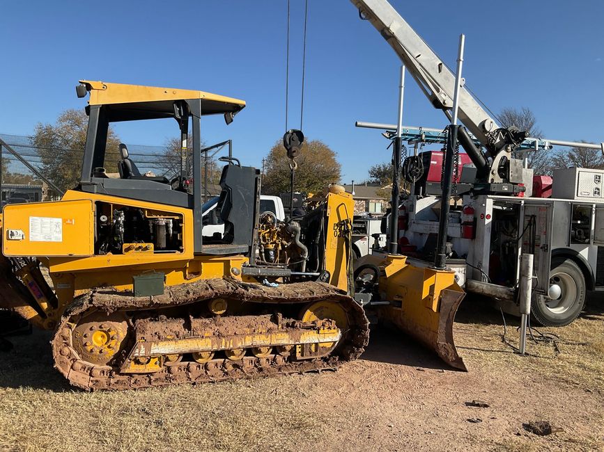 Yellow bulldozer with tracks and blade parked beside a crane truck on gravel lot