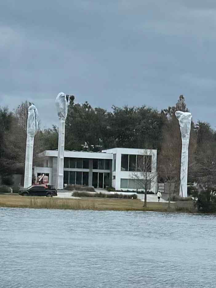 Modern white house with tall palm trees protected and covered for incoming freezing temperatures. Black car in driveway.