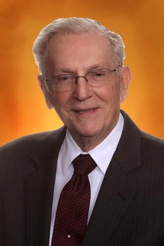 Studio portrait of an older man in a suit and tie, smiling against an orange gradient background