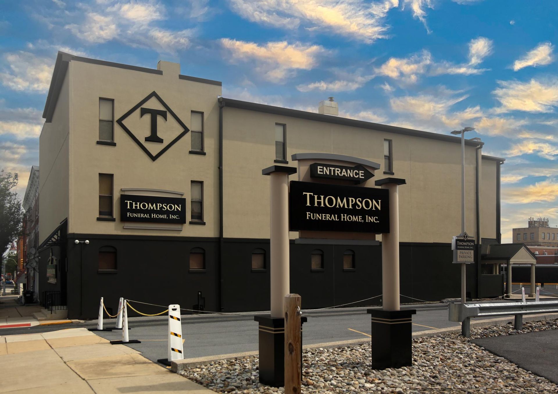 Tan building with Thompson restaurant sign and a T logo under a cloudy sky