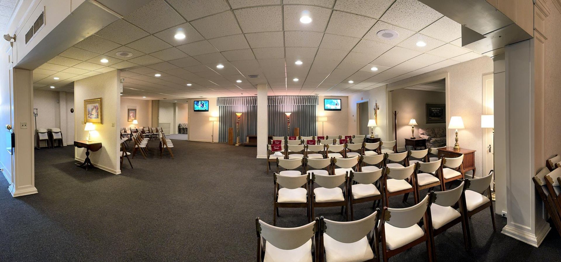 Wide conference hall with rows of white-covered chairs facing a stage, lit by ceiling lights