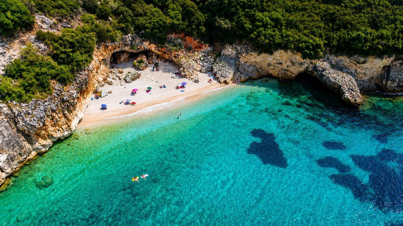Secluded sandy cove with turquoise water, rocky cliffs, and a few beachgoers