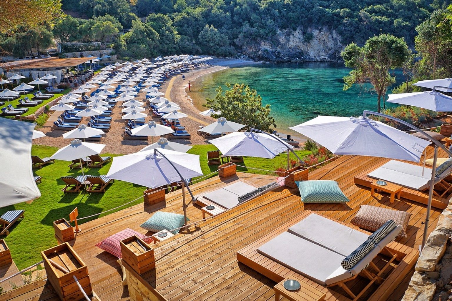 Sunny beach resort with white umbrellas, lounge chairs, and a turquoise bay backed by green cliffs