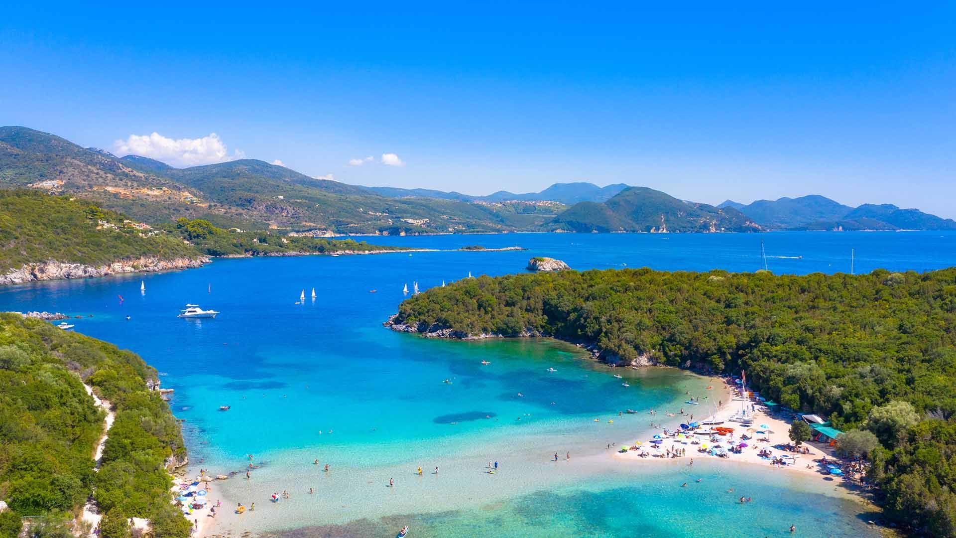 Tropical bay with turquoise water, sandy beaches, green islands, and distant mountains under a clear blue sky